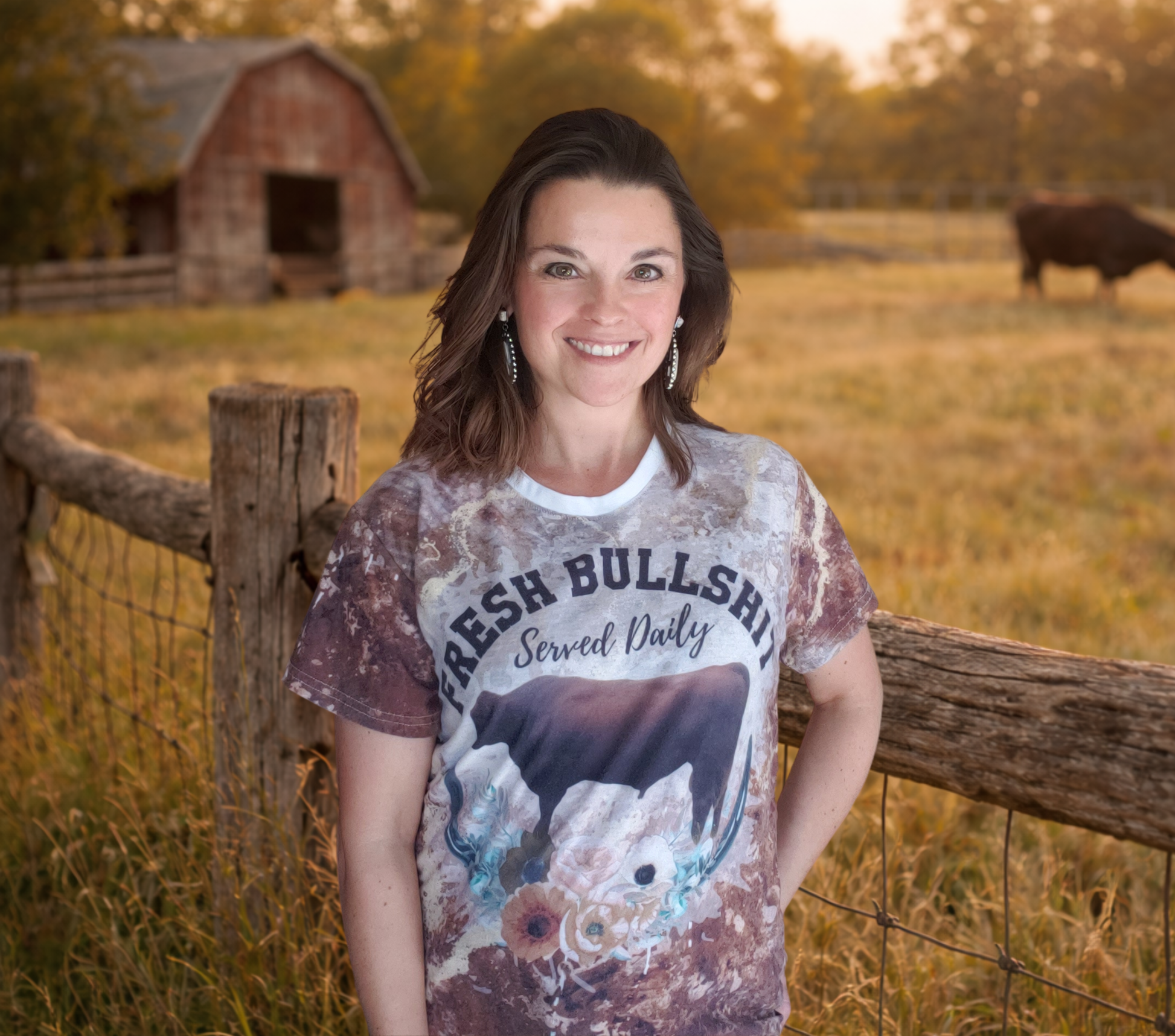 Woman wearing a graphic t-shirt in a rural setting with a barn and cow in the background.