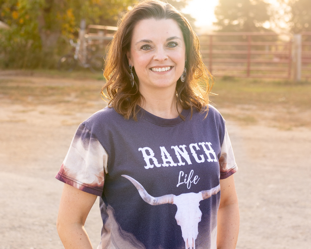 Woman wearing a 'Ranch Life' t-shirt with a longhorn skull design outdoors.
